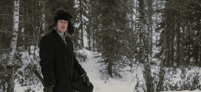 Mies seisoo lumihangessa kirveen kanssa. Hän on ollut tekemässä puita.